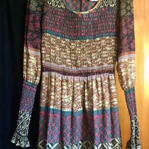 May include: A long-sleeved dress with a colorful, geometric pattern. The dress has a gathered bodice and a flowing skirt. The fabric is sheer and has a slightly textured finish.