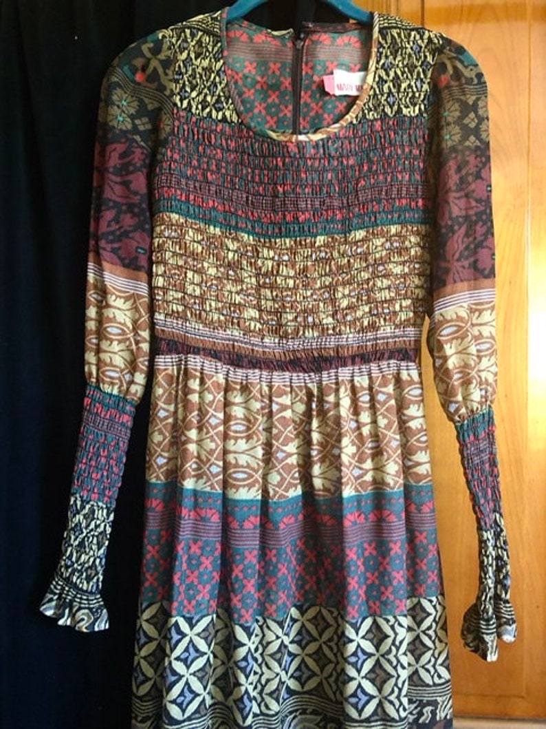 May include: A long-sleeved dress with a colorful, geometric pattern. The dress has a gathered bodice and a flowing skirt. The fabric is sheer and has a slightly textured finish.