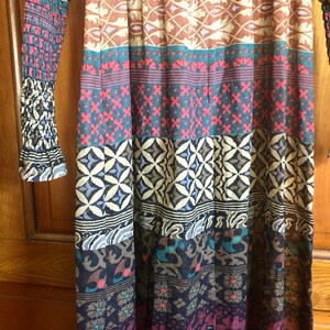 May include: A long, flowing dress with a colorful, patterned design. The dress has a fitted bodice and a flowing skirt with multiple layers of fabric. The pattern features a variety of geometric shapes and floral motifs in shades of brown, blue, red, and white.