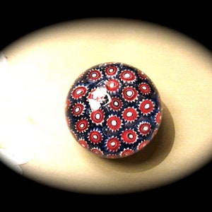 May include: A glass paperweight with a red and blue pattern of small circles. The paperweight is round and has a glossy finish.