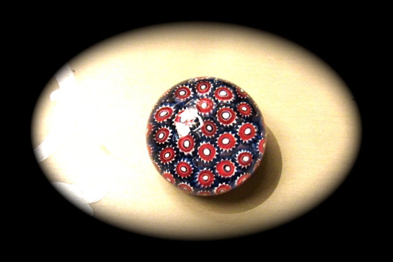 May include: A glass paperweight with a red and blue pattern of small circles. The paperweight is round and has a glossy finish.