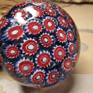May include: A glass paperweight with a swirling pattern of red, white, and blue. The paperweight is round and has a smooth, shiny surface.