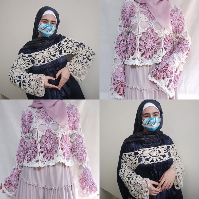 May include: A handmade crochet bolero in white and light purple, featuring a floral design. The bolero has long, bell sleeves and is worn over a dark blue dress. The crochet work is intricate and detailed, showcasing the craftsmanship.