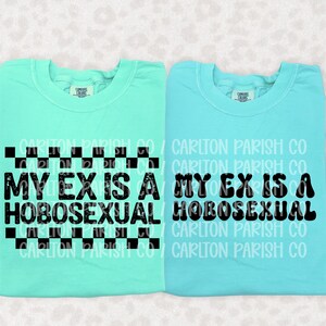 May include: Two crewneck t-shirts in mint and light blue. The mint shirt features a black checkered border and the text "MY EX IS A HOBOSEXUAL" in a distressed font. The light blue shirt displays the same text in a smooth, bold black font.