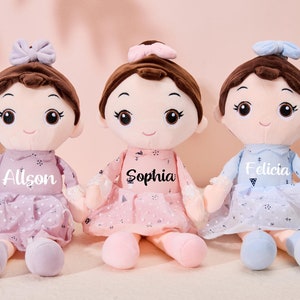 May include: Three plush dolls with brown hair, wearing dresses and bows. The dolls are named Allison, Sophia, and Felicia.