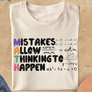 May include: A cream-coloured t-shirt with the text "MISTAKES ALLOW THINKING TO HAPPEN" in various colours. Mathematical formulas and equations are also printed on the shirt. Blue jeans and a brown hat are also in the image.