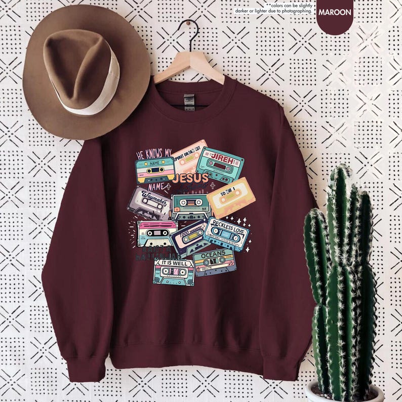 May include: Maroon sweatshirt with a graphic of vintage cassette tapes with Christian song titles printed on them. The titles include "He Knows My Name", "Waymaker", "Jesus", "Jireh", "So Am I", "Reckless Love", "It Is Well", and "Oceans".