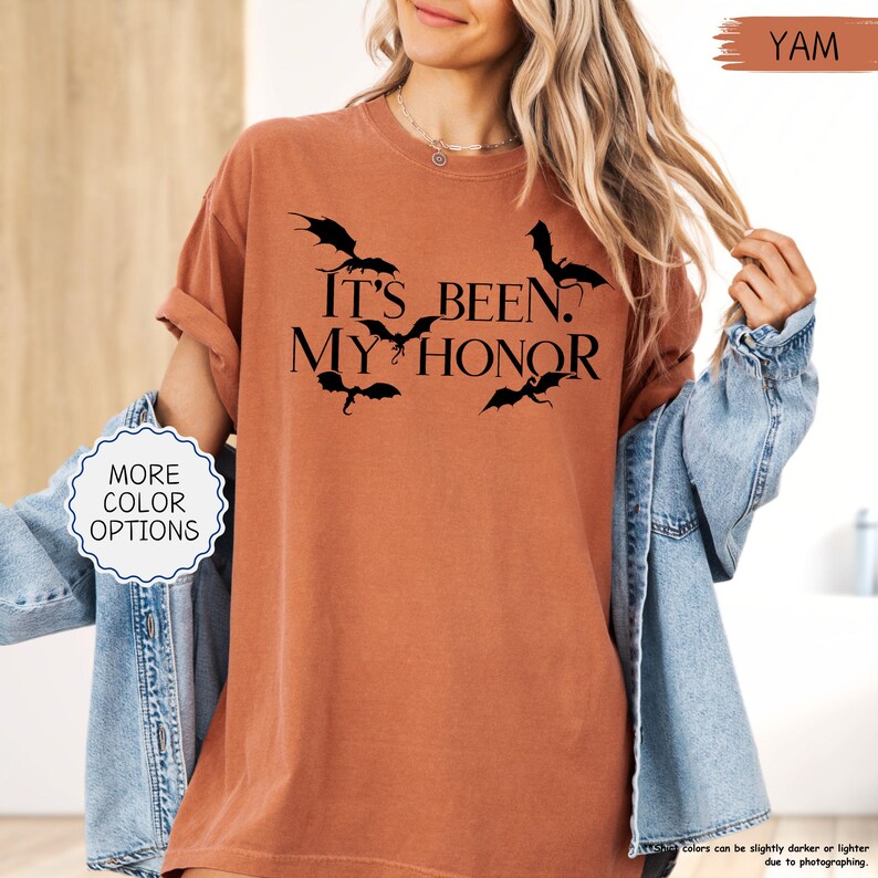 Pu&ograve; includere: Una maglietta color igname con la frase nera "IT'S BEEN. MY HONOR" e sagome di pipistrelli. La maglietta ha le maniche arrotolate ed &egrave; abbinata a una giacca di jeans. Un pulsante indica "MORE COLOR OPTIONS".