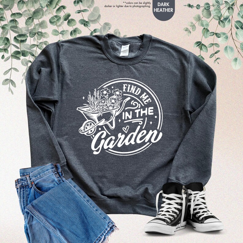 Puede incluir: Sudadera gris oscuro jaspeada con un gr&aacute;fico blanco de una carretilla llena de flores y el texto "Find me in the garden".
