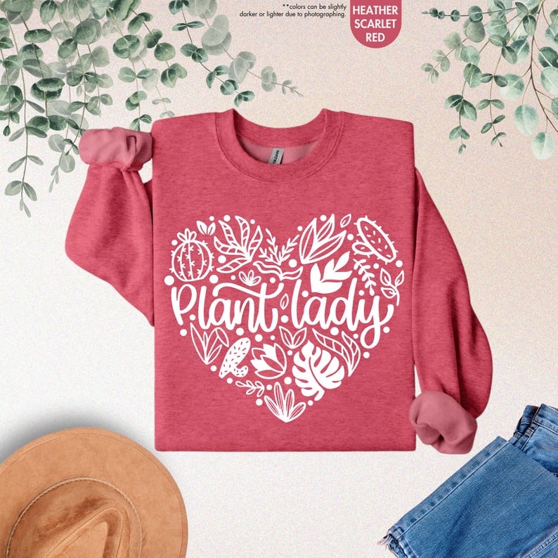 May include: A heather scarlet red sweatshirt with a white heart-shaped design featuring the text "Plant lady" surrounded by various plant illustrations.
