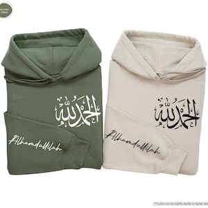 May include: Two hooded sweatshirts, one military green and one sand-colored. Each features Arabic calligraphy and the word "Alhamdullilah" in script. The sweatshirts are displayed on a white background.