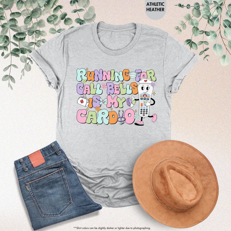 May include: A light gray t-shirt with the text "Running for call bells is my cardio" in colorful letters. A cartoon illustration of a call bell with a nurse's cap is holding a stethoscope.
