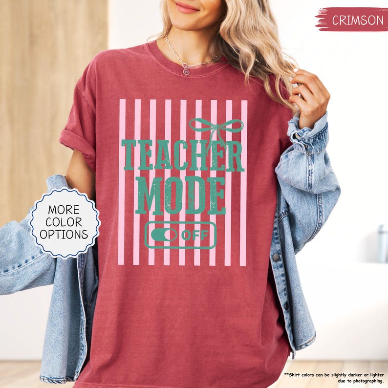 May include: Crimson-colored t-shirt with the text "TEACHER MODE OFF" in teal, set against a pink and white striped background. The shirt has a relaxed fit and rolled-up sleeves. The words "MORE COLOR OPTIONS" are in a white circle.