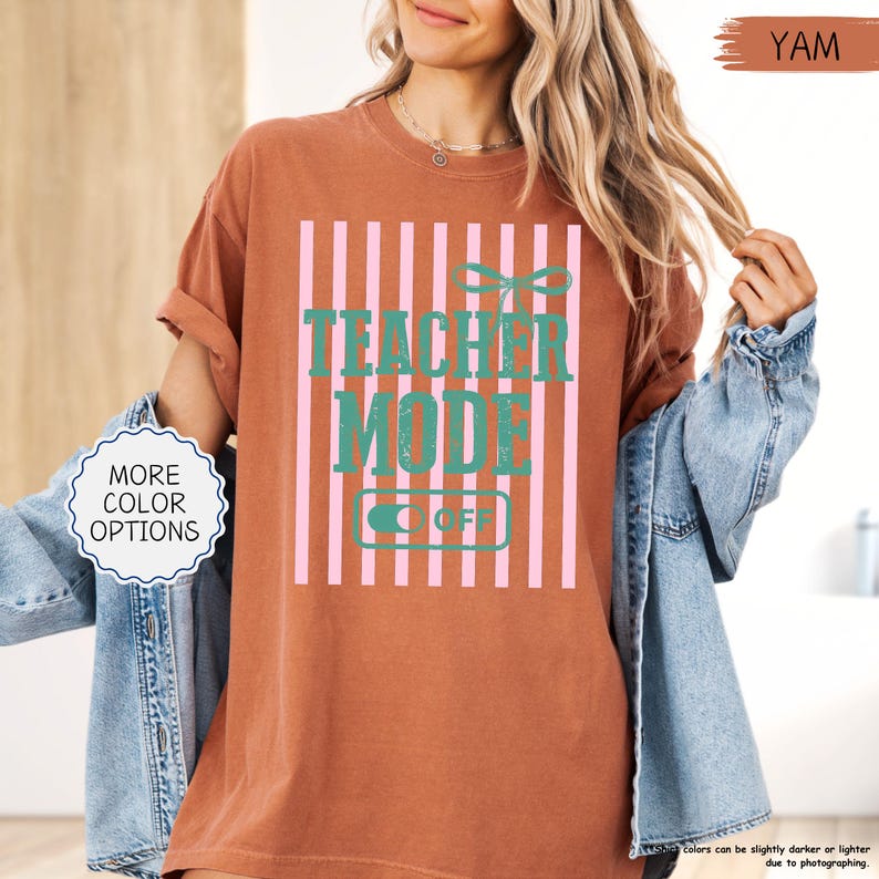 May include: A yam-colored t-shirt with a vertical pink and white striped design. The shirt features the text "TEACHER MODE OFF" in teal. A button on the shirt says "OFF". The shirt is a casual style.