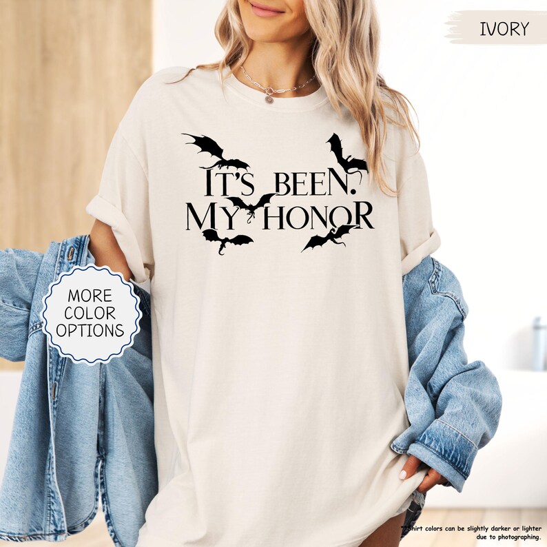 Pu&ograve; includere: T-shirt color avorio con la scritta nera "It's Been. My Honor" e sagome di draghi neri. La maglietta &egrave; indossata con una giacca di jeans. L'immagine include anche un pulsante con "More Color Options".