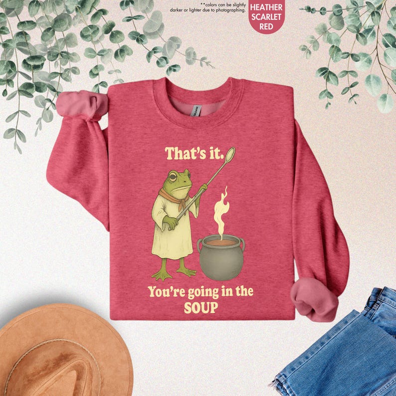 Pu&ograve; includere: Felpa rosso scarlatto melange con un'illustrazione di uno chef rana. La rana sta mescolando una pentola di zuppa con il testo "That's it. You're going in the SOUP" stampato sotto.