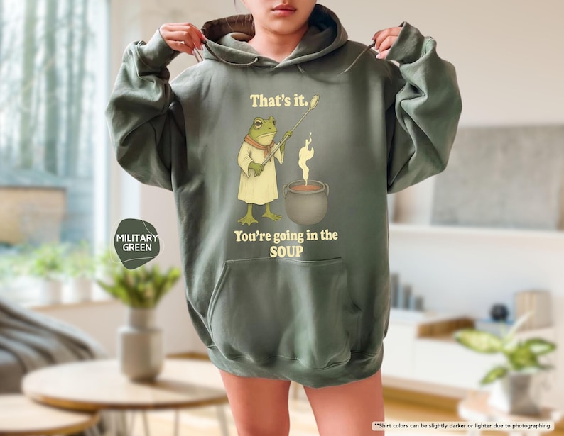 Pu&ograve; includere: Felpa con cappuccio verde militare con una grafica di una rana che tiene un mestolo sopra una pentola di zuppa. Il testo sulla felpa recita: "That's it. You're going in the SOUP."