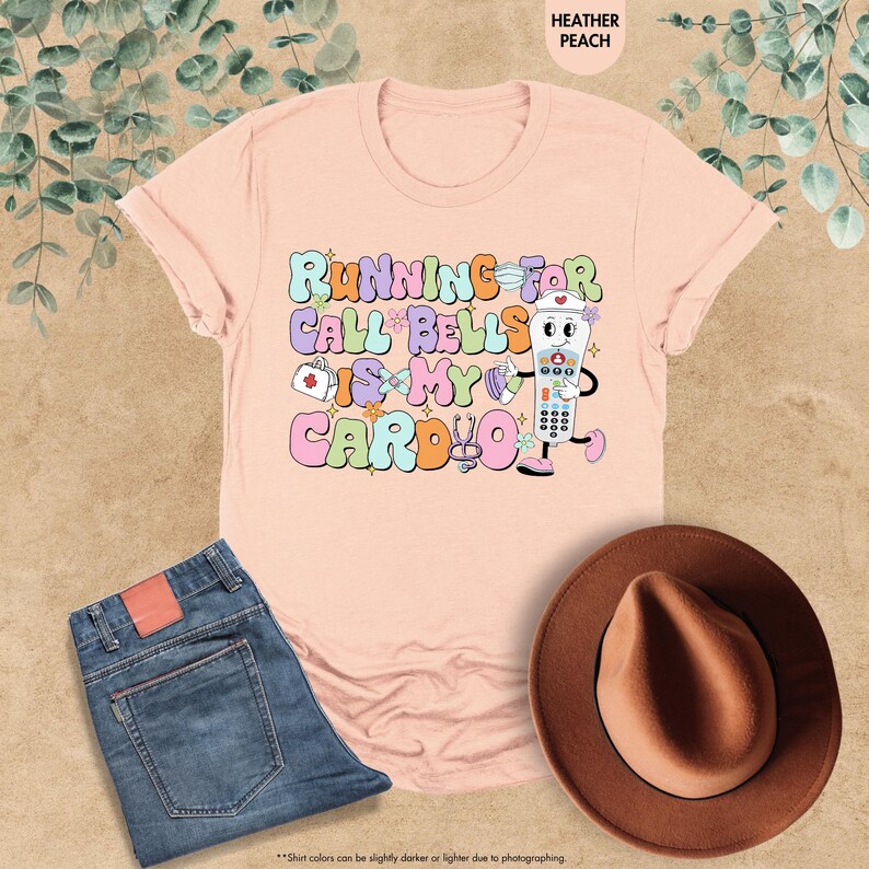 May include: A pink t-shirt with the text "Running for call bells is my cardio" in colorful letters. A cartoon illustration of a call button with a nurse's cap and a stethoscope is next to the text.