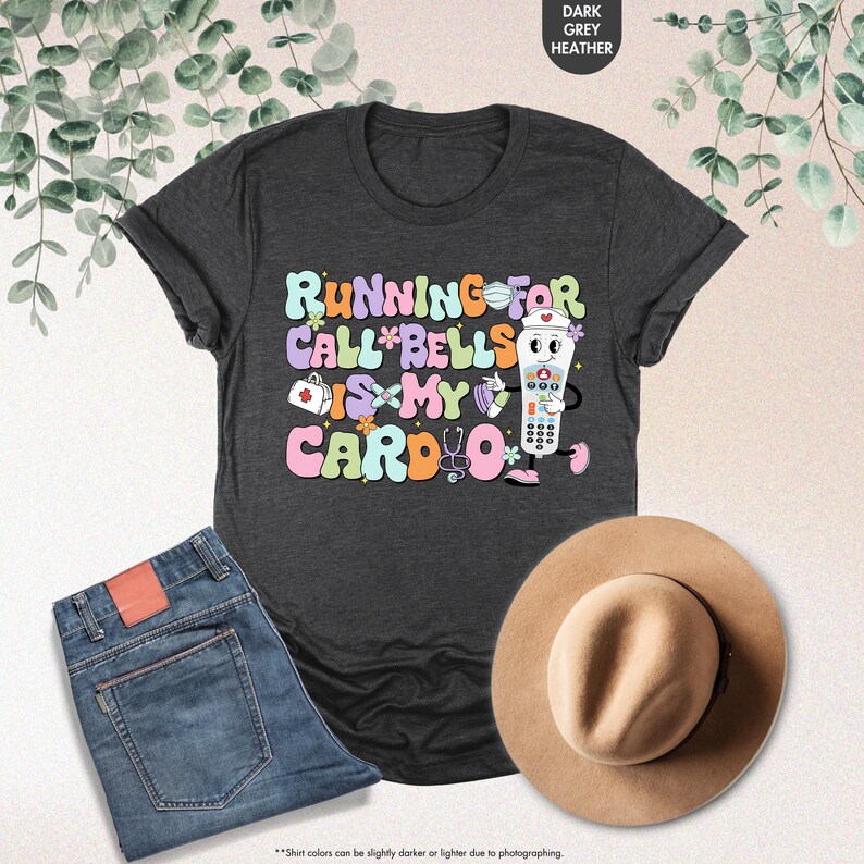 May include: A dark heather grey t-shirt with a graphic of a nurse holding a call button. The text on the shirt reads "Running for call bells is my cardio".