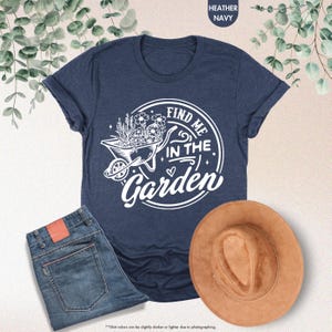 Puede incluir: Una camiseta azul marino con un gr&aacute;fico blanco de una carretilla llena de flores y el texto "Find me in the Garden".