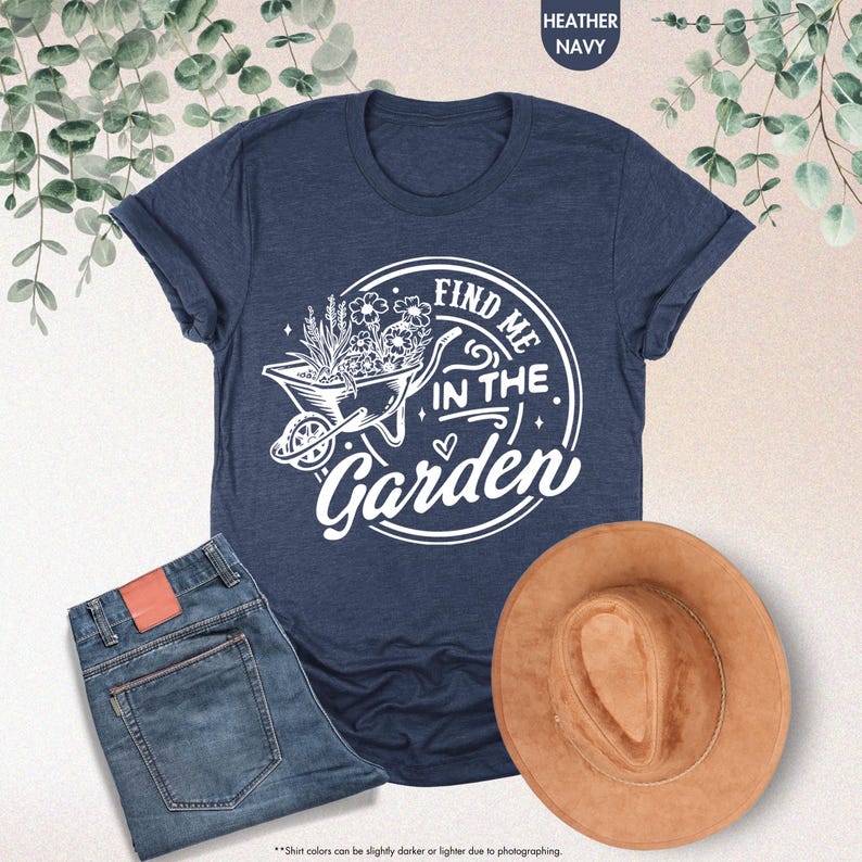 Puede incluir: Una camiseta azul marino con un gr&aacute;fico blanco de una carretilla llena de flores y el texto "Find me in the Garden".