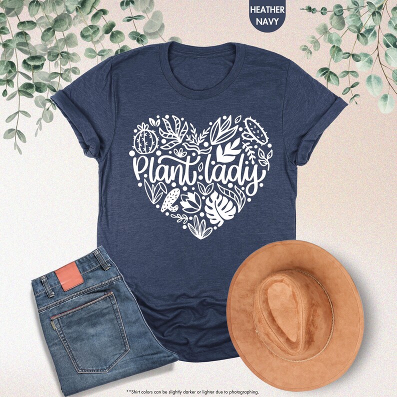 May include: A navy blue t-shirt with a white heart design featuring the text "Plant lady" surrounded by stylized plants and flowers.