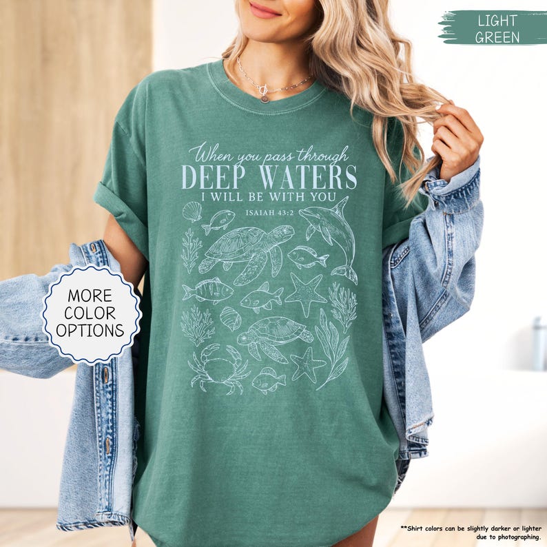 May include: Light green t-shirt with the text "When you pass through deep waters, I will be with you" and a sea life graphic. The shirt also has the text "Isaiah 43:2". The shirt has a round neck and short sleeves.