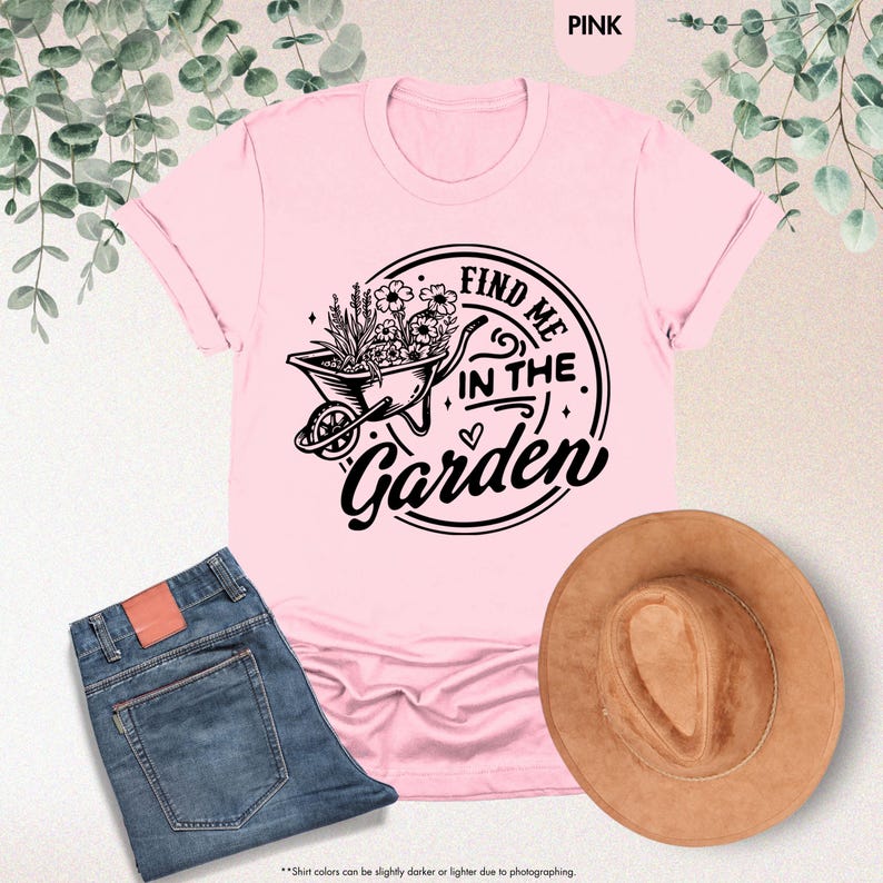 Puede incluir: Camiseta rosa con un gr&aacute;fico negro de una carretilla llena de flores y el texto "Find Me In The Garden".