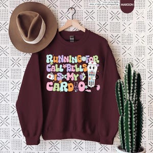May include: Maroon sweatshirt with a graphic of a nurse's call button with the text "Running for call*bells is my cardio*"