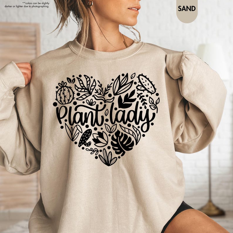 May include: A beige sweatshirt with a black heart-shaped design featuring a variety of plants and the text "Plant Lady".
