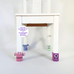 May include: A white wooden chair with four colorful, crocheted monster leg warmers. The monsters are pink, purple, blue, and green, each with unique features. Text on the chair reads, "Check item description for size information."