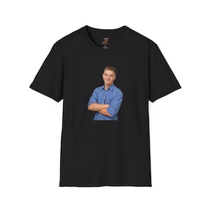 May include: A black t-shirt featuring a photograph of a person wearing a blue button-down shirt. The person is smiling and has their arms crossed.