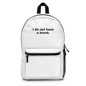 May include: White backpack with black detailing, including a top handle, zip pulls, and a mesh side pocket. The front pocket has a black zip. The text "I do not have a bomb." is printed on the front of the backpack.