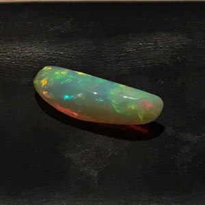 May include: A light green and white opal gemstone with iridescent flashes of color. The opal is oval shaped and has a smooth, polished surface.