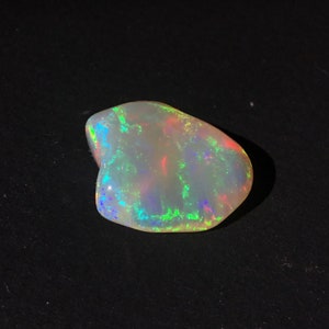 May include: A white opal gemstone with green, blue, and red iridescent flashes. The opal is irregularly shaped and has a smooth, polished surface.