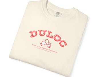 May include: Cream-colored t-shirt with the word "DULOC" in red, arched across the top. Below, it reads "home of the fighting farquaads" and "things are looking up" in red. Two boxing gloves are in the center.