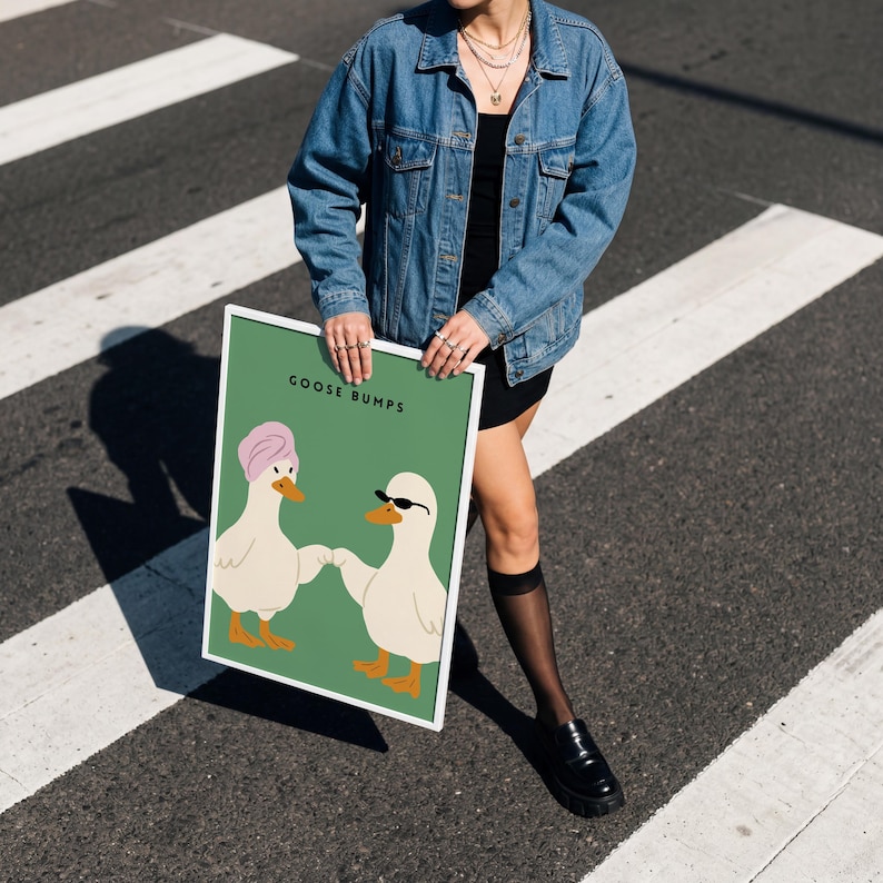 May include: A framed art print featuring two cartoon geese on a green background. One goose wears a pink towel, the other sunglasses. The words "GOOSE BUMPS" are printed at the top. The frame is white.