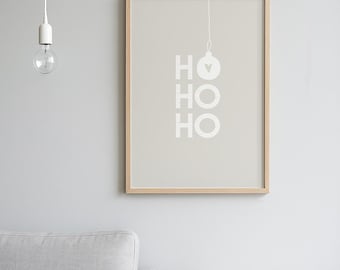 May include: A framed print with the text "HO HO HO" in white, with a Christmas ornament graphic. The print is in a light wood frame and hangs on a gray wall. A light bulb hangs from the ceiling.
