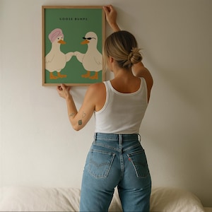 May include: A framed art print with the text "GOOSE BUMPS" above a cartoon illustration of two ducks. One duck wears a pink turban, the other sunglasses. The background is green, and the frame is wood.
