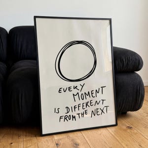 Könnte beinhalten: Ein gerahmtes, rechteckiges Wandbild mit einer handgezeichneten, schwarzen, kreisförmigen Kritzelei auf cremefarbenem Hintergrund. Unter dem Kreis steht der Text: EVERY MOMENT IS DIFFERENT FROM THE NEXT in einer lockeren, schwarzen Handschrift.