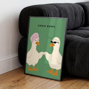 May include: Framed art print featuring two cartoon geese on a green background. One goose wears a pink turban, the other sunglasses. The text "GOOSE BUMPS" is at the top. The geese are holding hands. The frame is black.