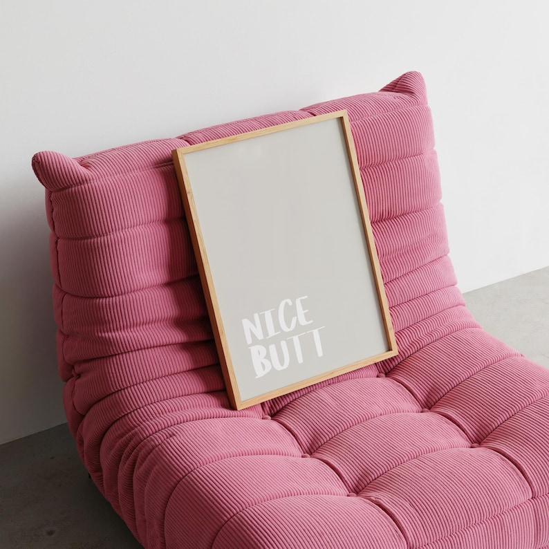 Modern wall art poster with a simple white background and light grey text reading “Nice Butt.” The design is minimalist, focusing on typography and negative space. Displayed in a lifestyle mockup, it complements Scandinavian and clean aesthetic interiors, making it ideal for stylish and understated home decor.