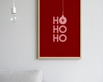 May include: A framed art print with a red background and the words "HO HO HO" in light pink. A pink ornament with a heart is above the first "HO". The print is in a wooden frame. The image is of a Christmas theme.