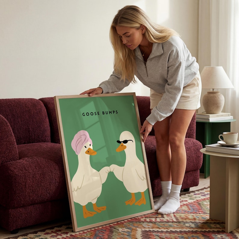 May include: A framed art print featuring two cartoon geese on a green background. One goose wears a pink towel, the other sunglasses. The text "GOOSE BUMPS" is at the top. The frame is a light brown color.
