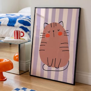 Op de afbeelding: Een ingelijste kunstdruk met een gestileerde bruine kat met zwarte lijndetails, gesloten ogen en oranje wangen, tegen een achtergrond van verticale lichtpaarse en crèmekleurige strepen. De kat heeft een rond lichaam en een simpele staart.
