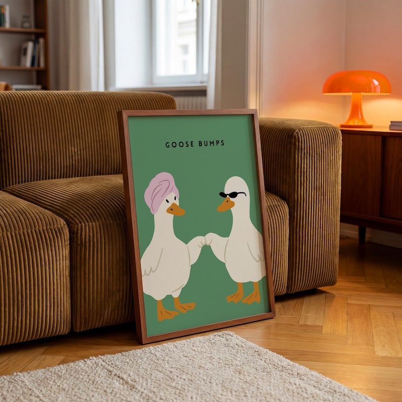 May include: A framed art print featuring two cartoon geese on a green background. One goose wears a pink turban, the other sunglasses. The text "GOOSE BUMPS" is at the top. The frame is brown.