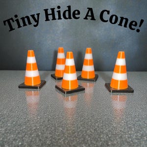 Könnte beinhalten: Fünf Miniatur-Leitkegel mit orangefarbenen und weißen Streifen auf schwarzen quadratischen Sockeln. Die Kegel sind in einer Reihe auf einer gesprenkelten grauen Oberfläche angeordnet. Der Text "Tiny Hide A Cone!" steht über den Kegeln.