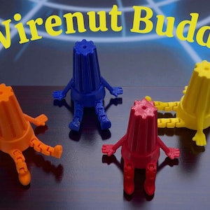 May include: Four colorful Wirenut Buddy figures in orange, blue, red, and yellow. Each figure has a conical body with a gear-like top and articulated arms and legs. The text "Wirenut Buddy" is in yellow above the figures.