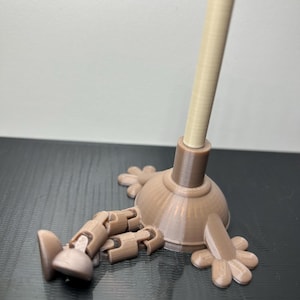 Op de afbeelding: Een grillig 3D-geprint beeldje met een zuigervormig lichaam, een lichtbruine handgreep en een donkerbruine basis. Het heeft beweegbare ledematen en bloemvormige voeten, wat het een speelse uitstraling geeft.