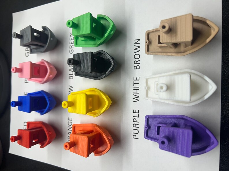 May include: A selection of miniature boats in a range of colours: grey, green, pink, black, blue, yellow, red, orange, brown, white, and purple. Each boat features a cabin and a cylindrical element.